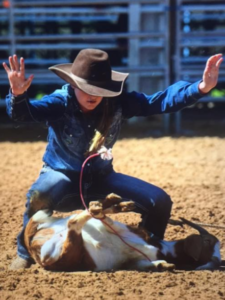 A cowgirl tying up a goat.