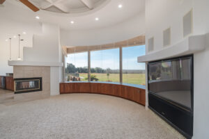 A circular living room with large windows and L-shaped fireplace.fire