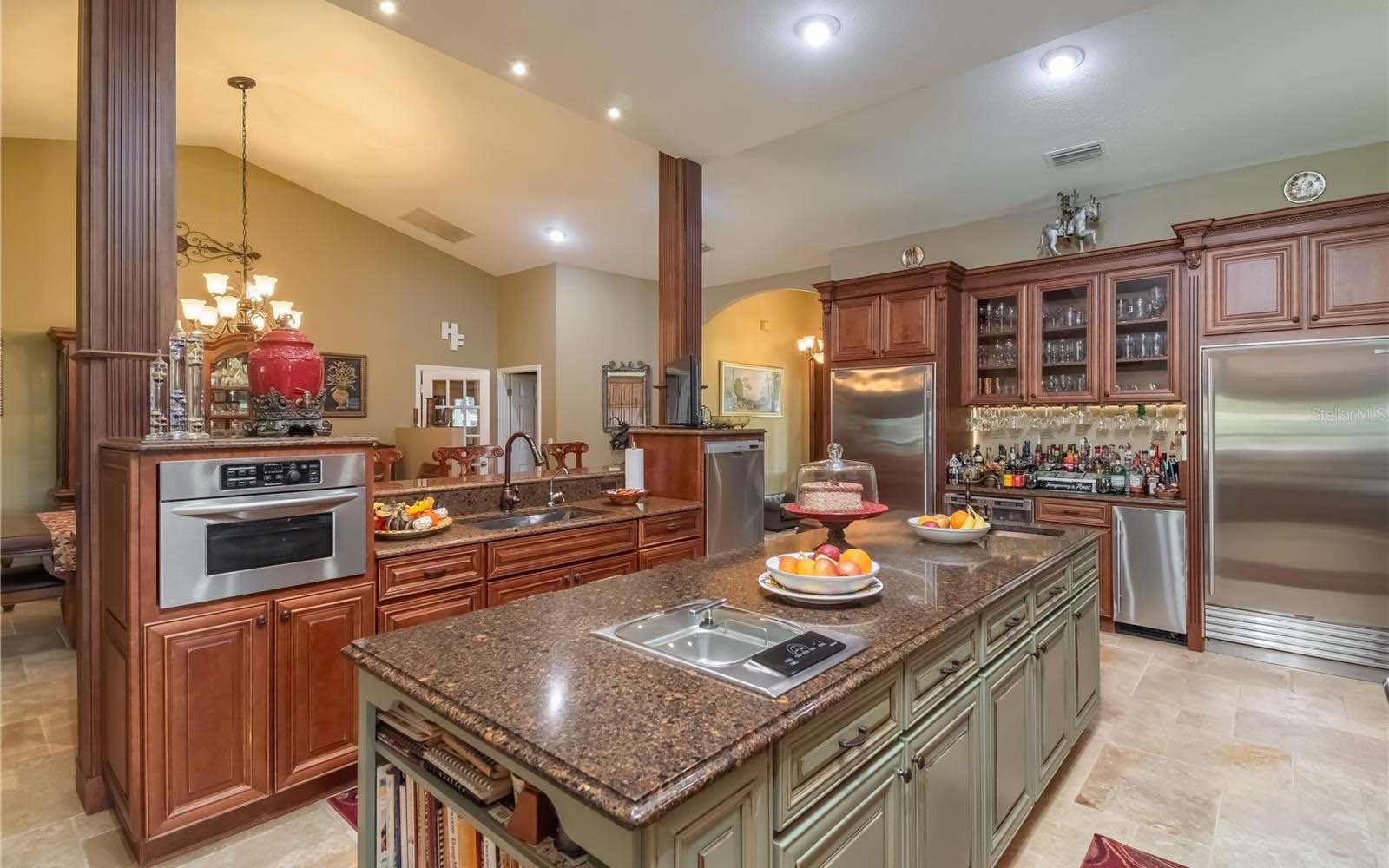 A beautiful kitchen with wood cabinetry, a brick oven alcove, and ornate pot rack.