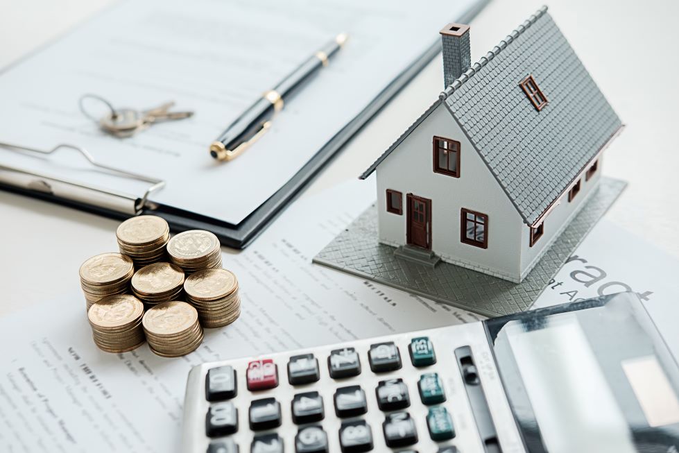 A calculator, coins, model house, and notepad and pen