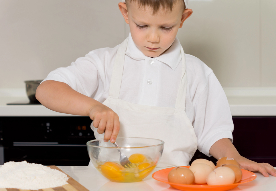 A boy cracking eggs to bake a cake.