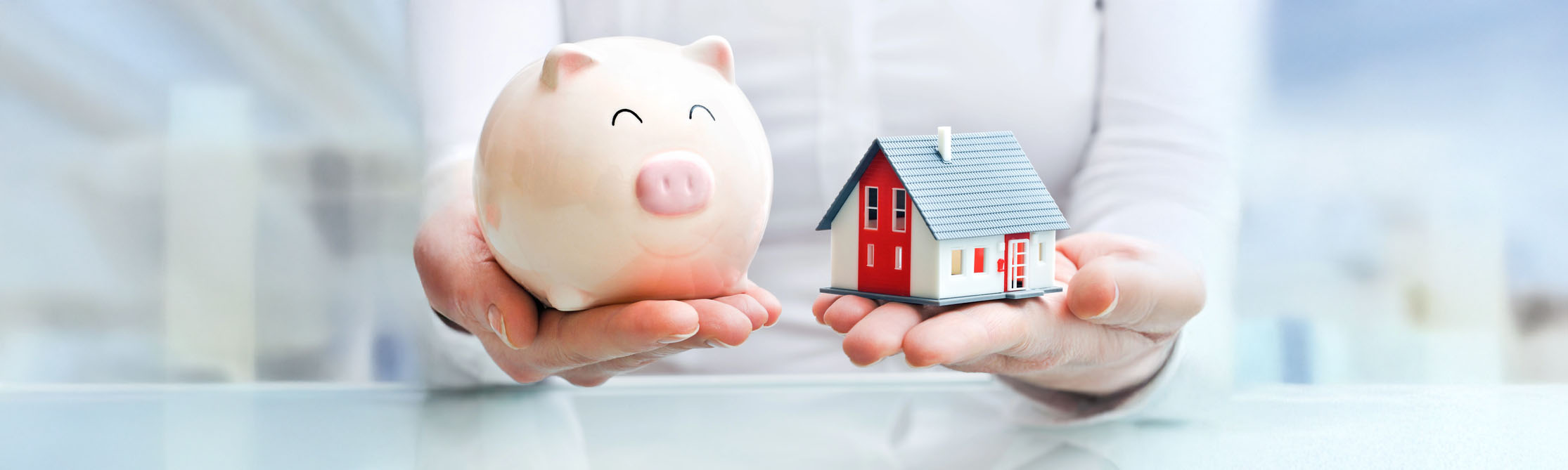 A person holding a piggy bank and a model house.